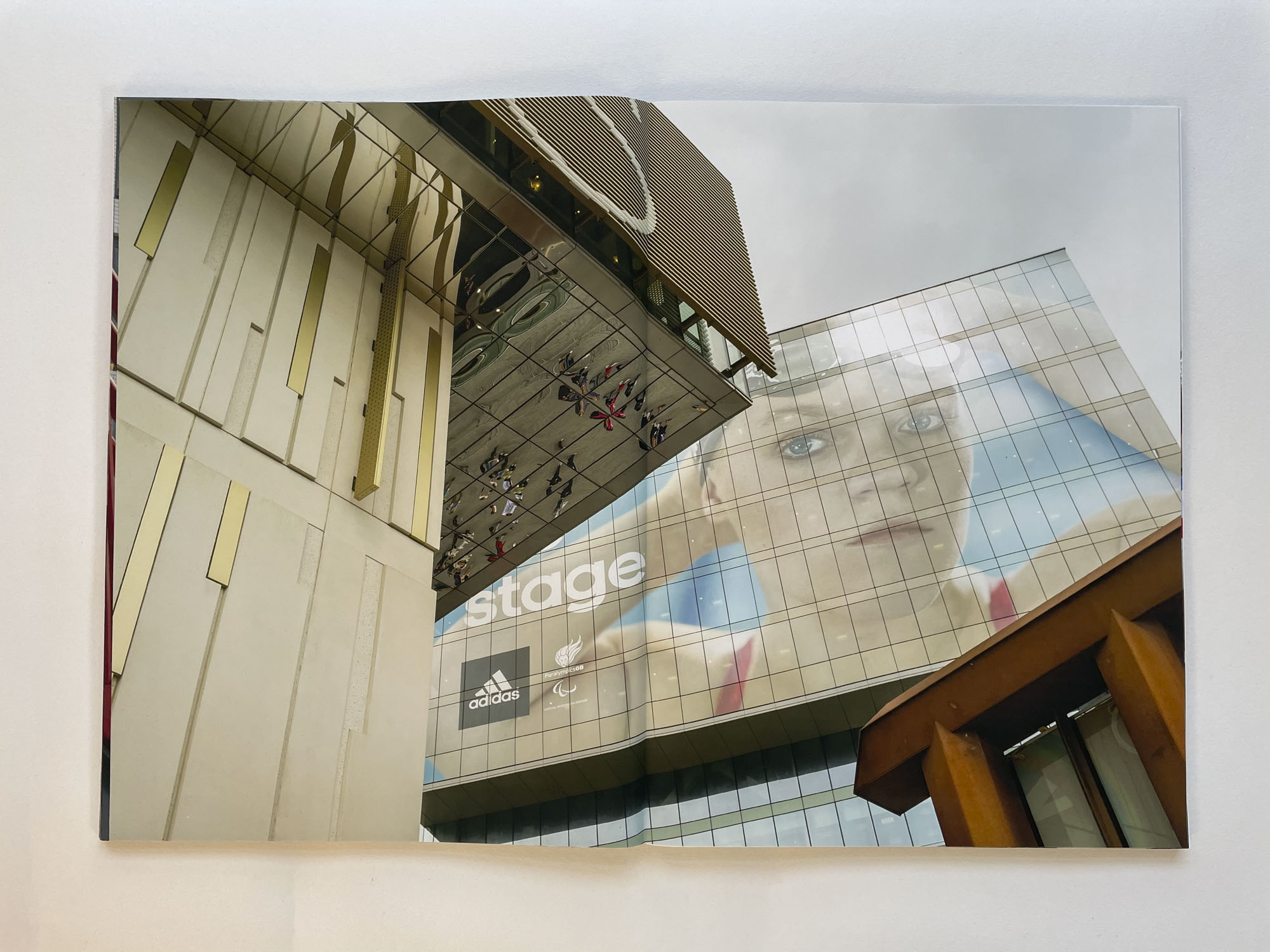looking up at the facade of two new buildings, on one the face of a swimmer looms large, on the underside of part of the other building can be seen the distorted reflections of people