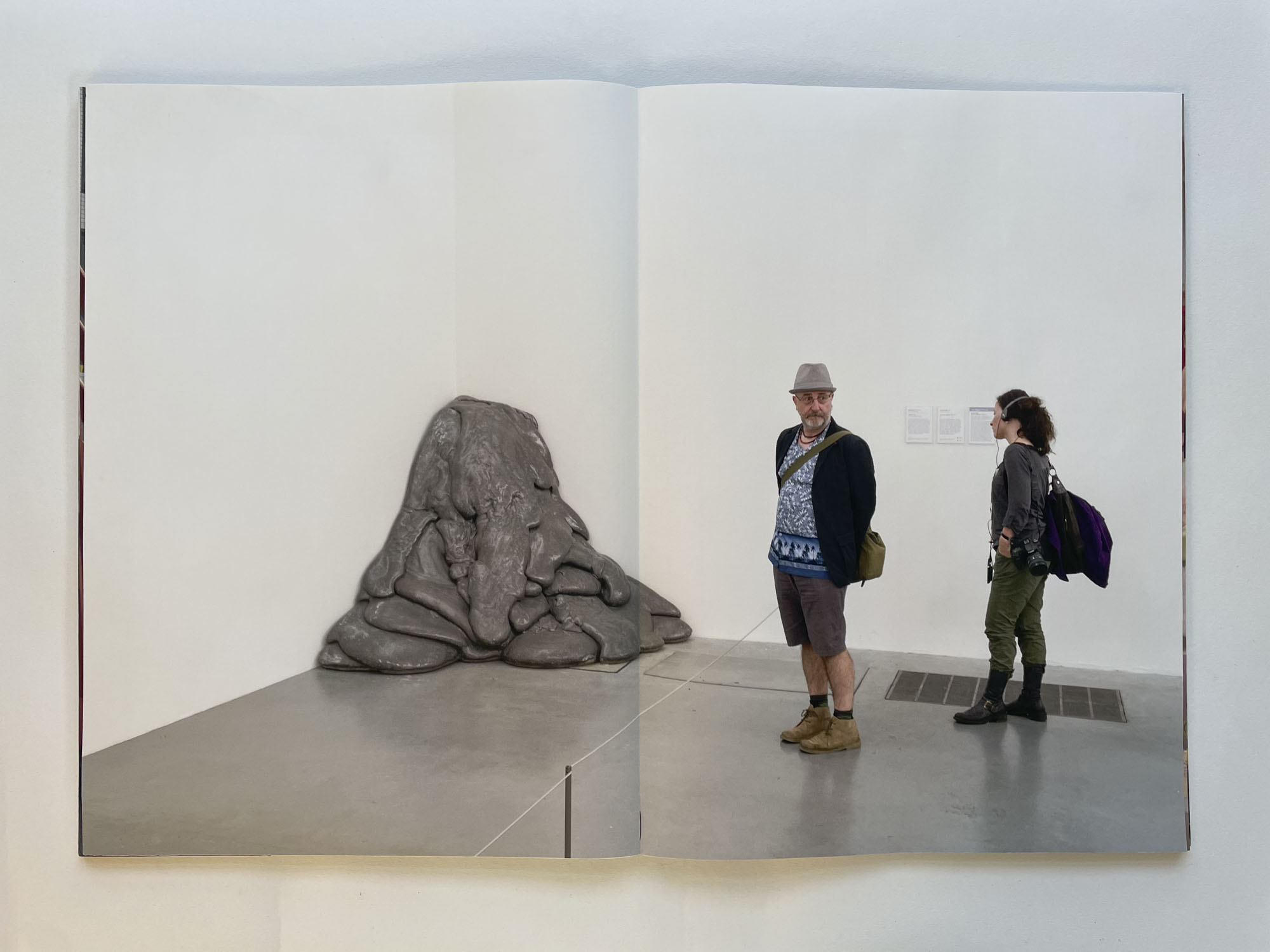 in the corner of an art gallery is a melted sculpture, one person looks at it, another looks away