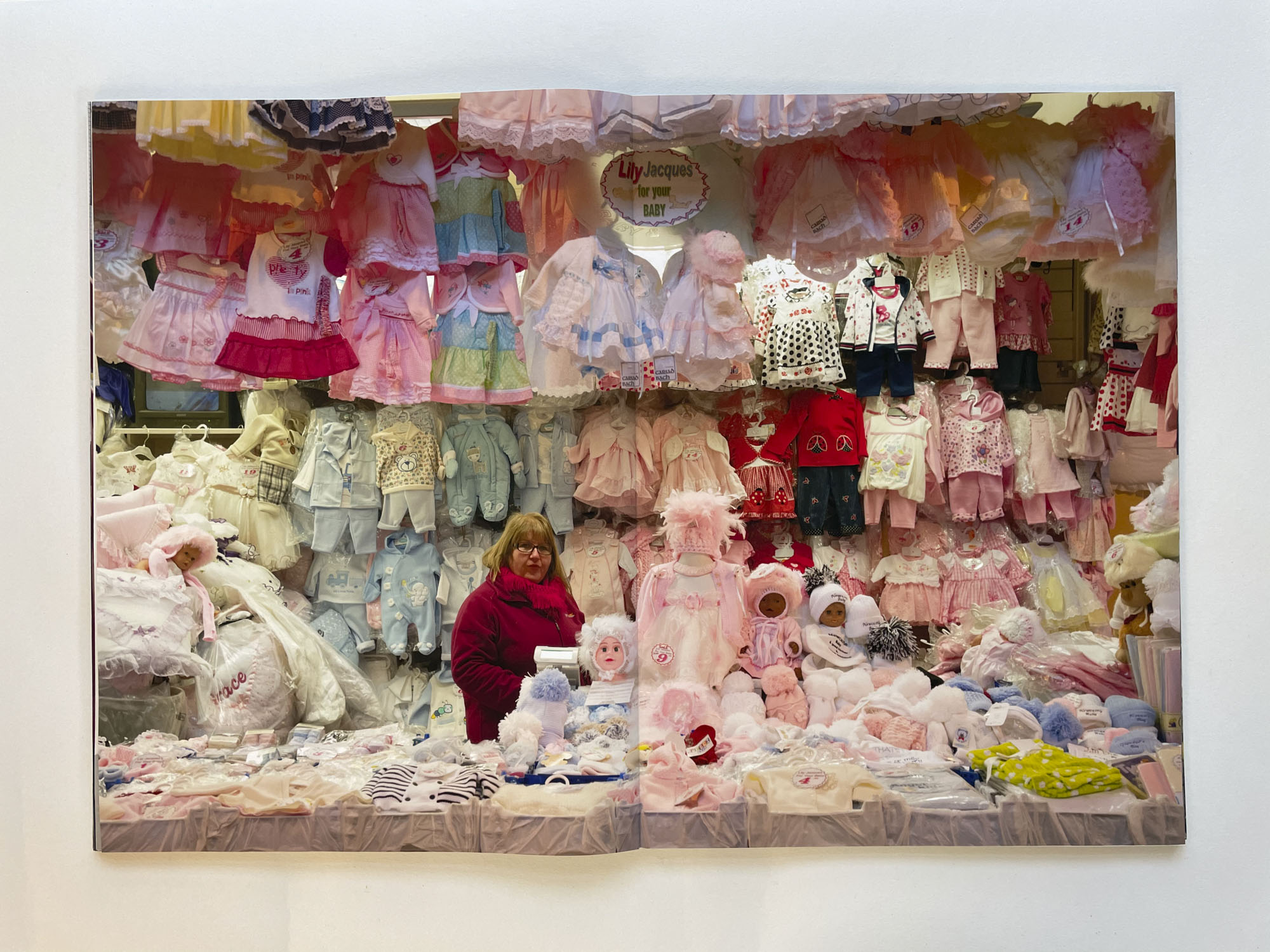 a large market stall absolutely full of blue and white baby clothes, at the centre stands a woman looking at the viewer