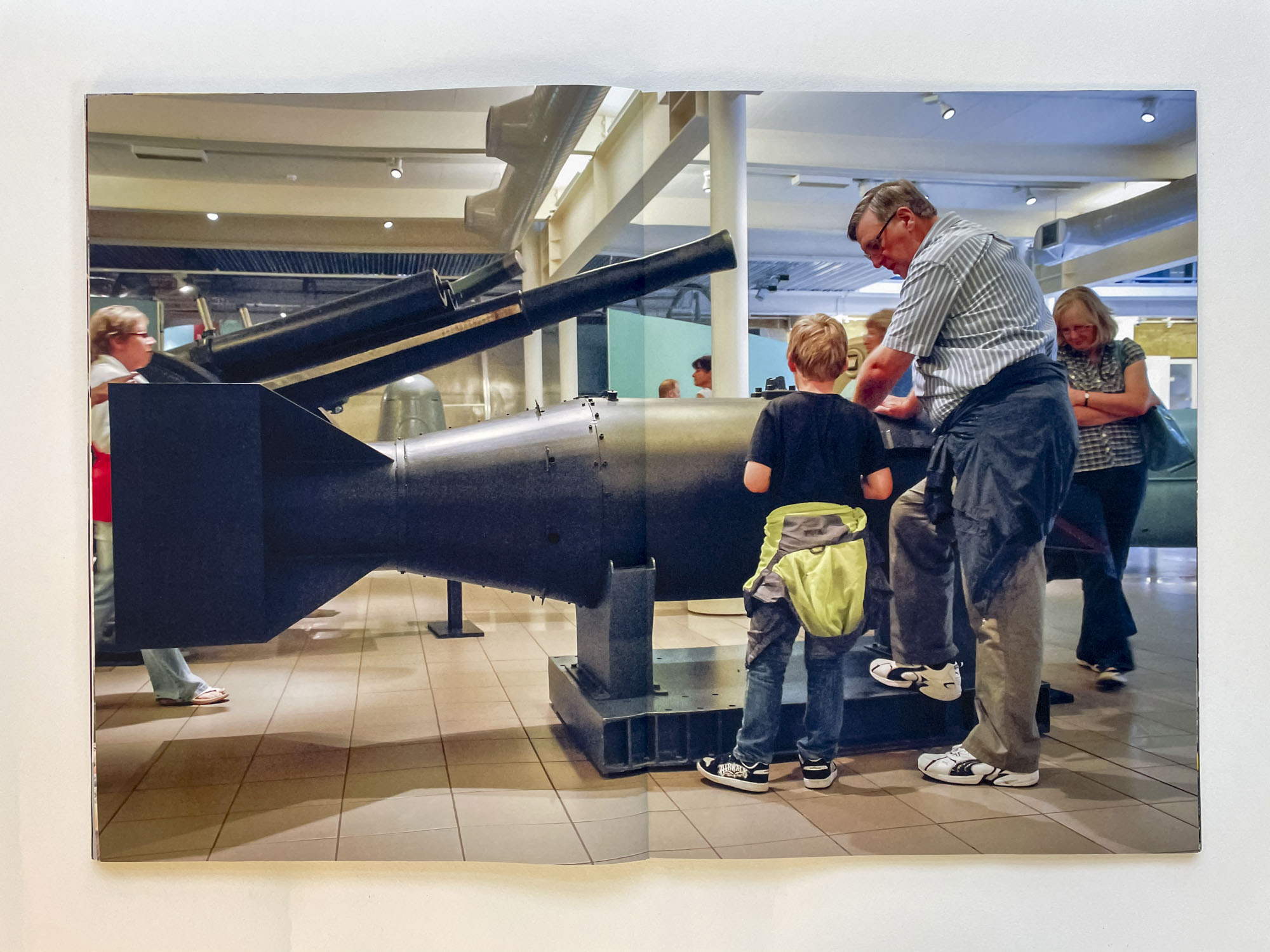 a large black bomb stands in a museum, a grandfather explains something to his young grandson while leaning on it