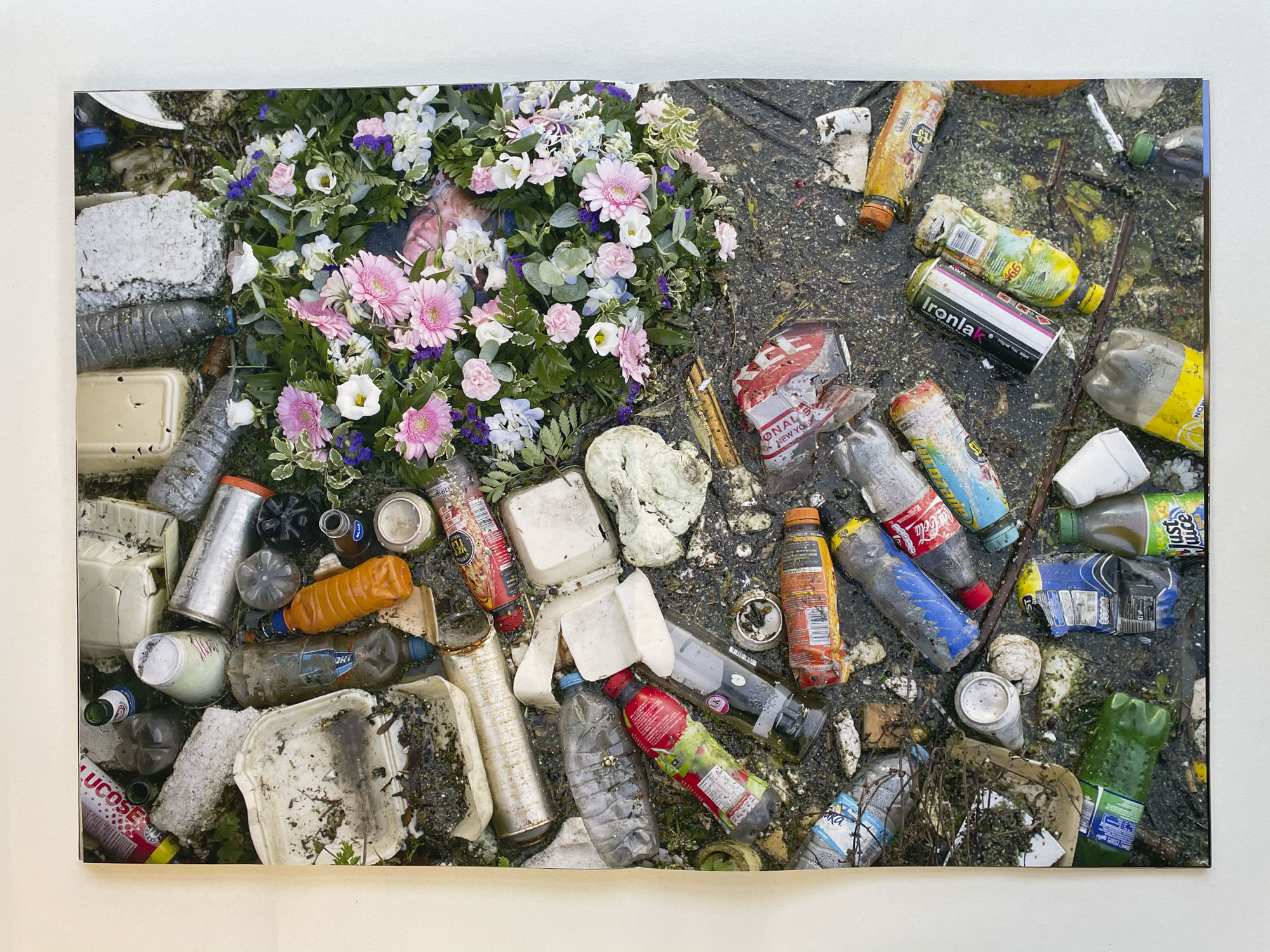 a large amount of plastic detritus floats on water, in one corner there is a plastic wreath, at the centre of which is a womans face