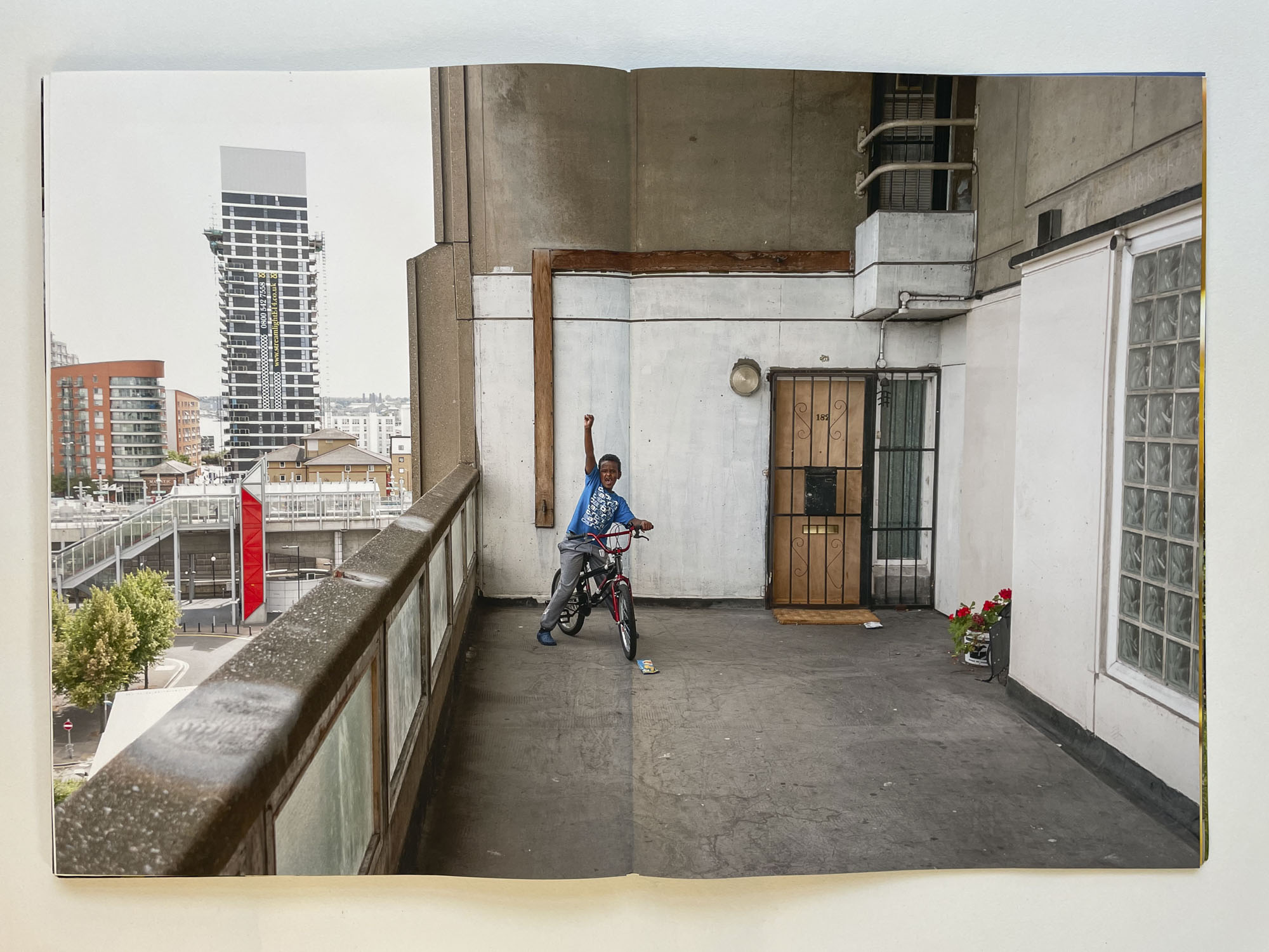 on the open deck of a council block, a young boy punches the air triumphantly while sitting on his bike