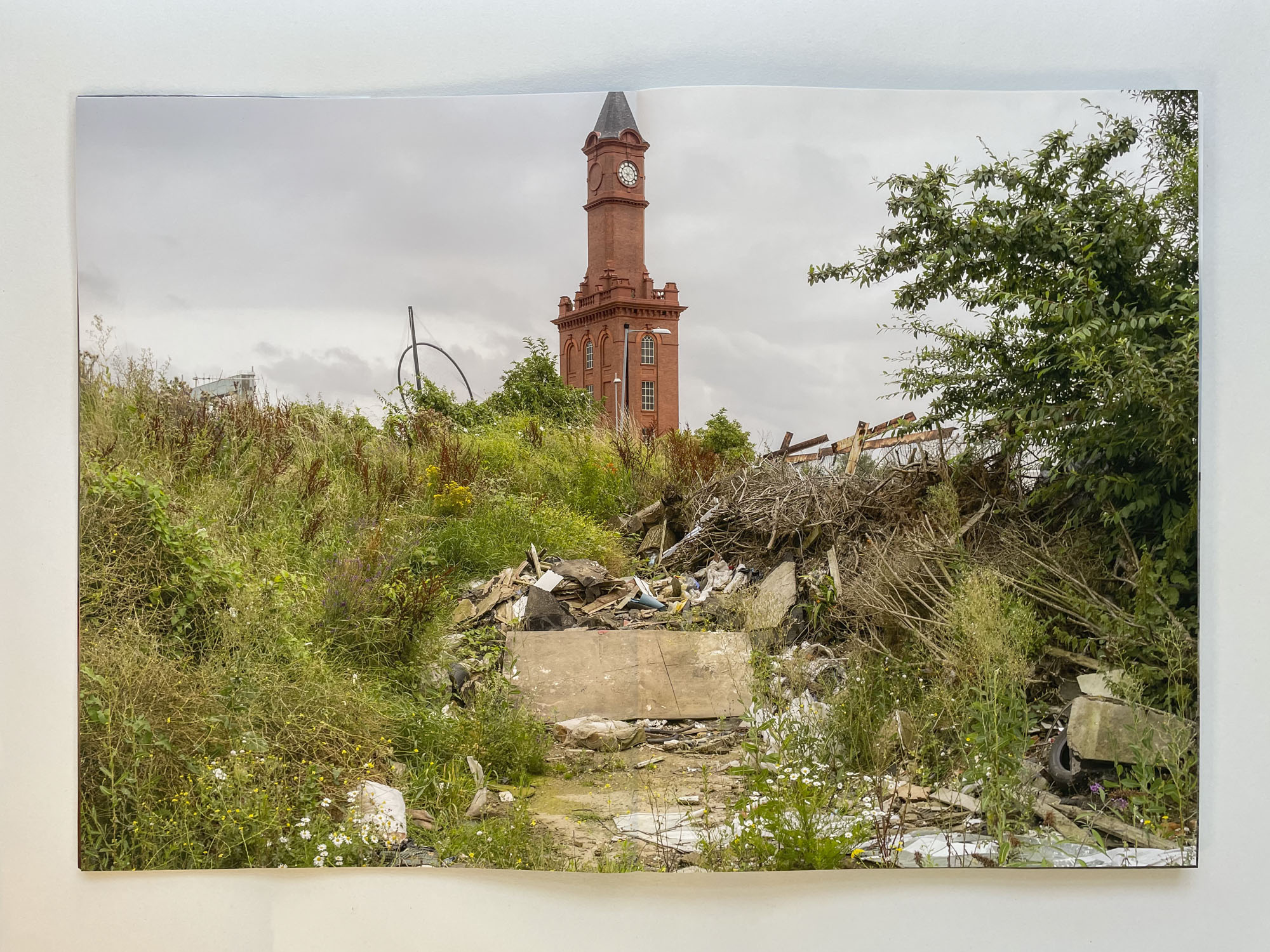 in the foreground detritus behind which a red brick clock tower rises against the sky, the clock faces are missing their hands