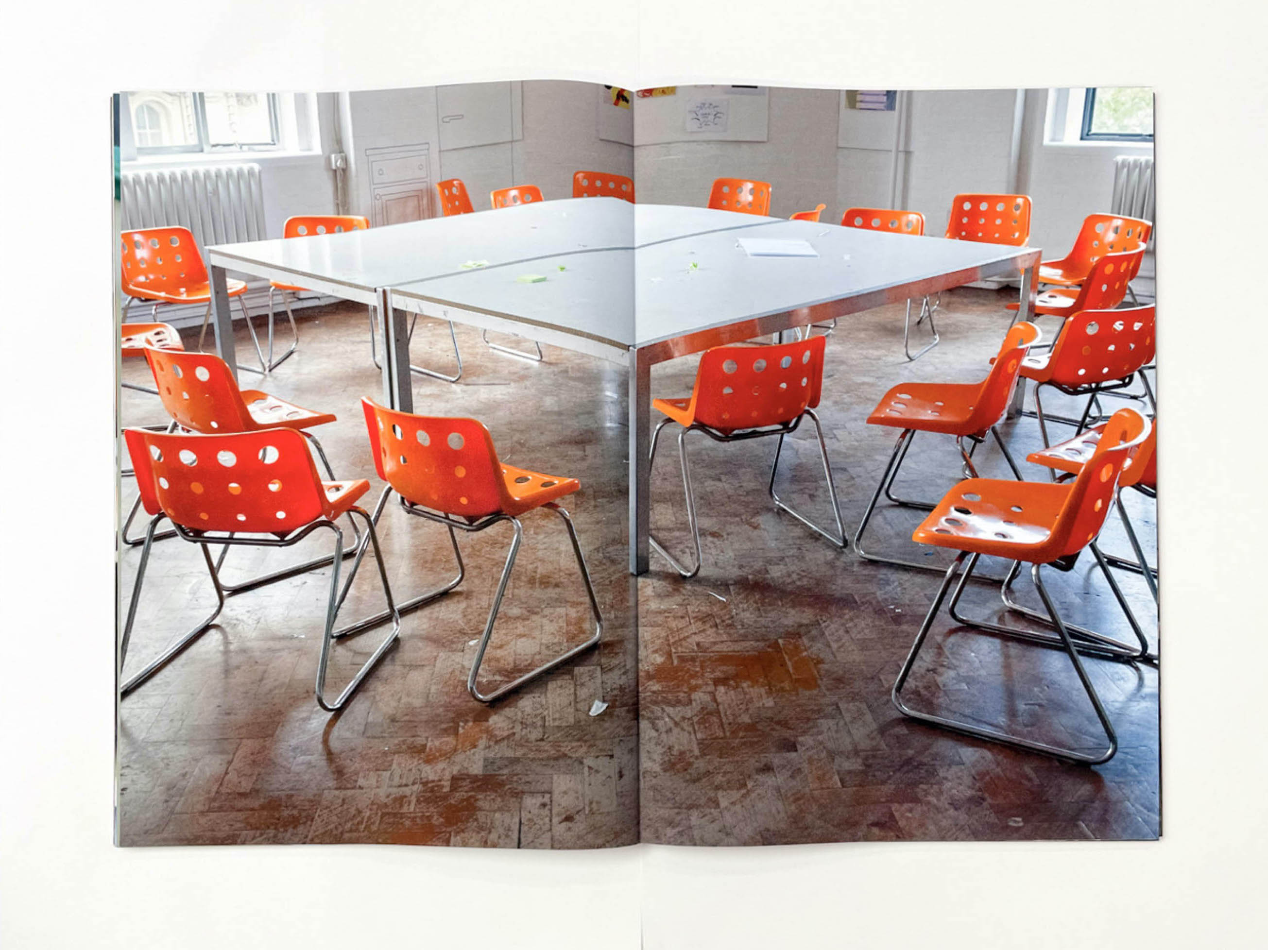 in a large room with a parquet floor many orange plastic chairs surround a large table