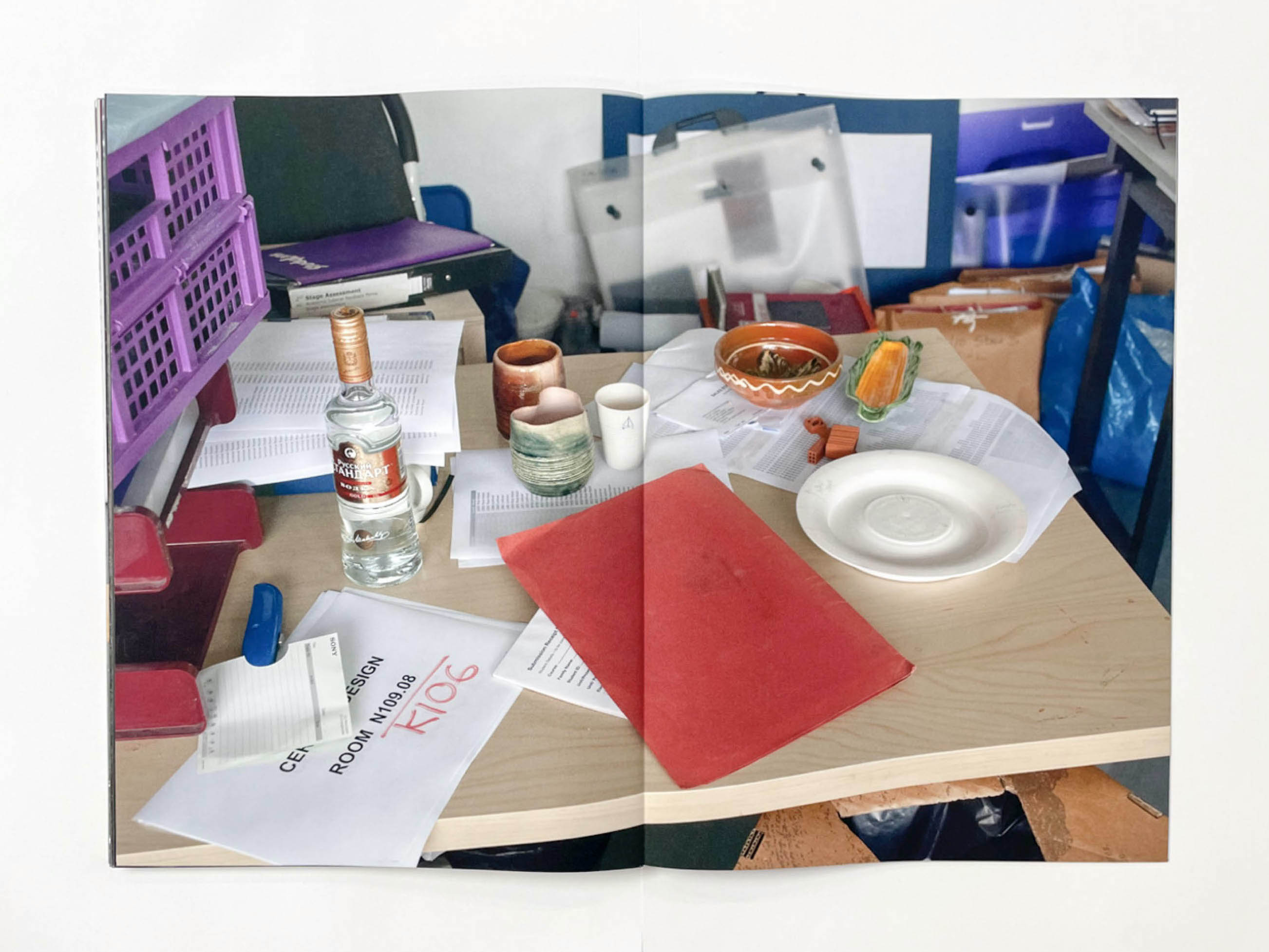 the chaotic contents of a table with a bottle of ouzo or vodka, cups and a piece of paper stating Ceramic Design room k106