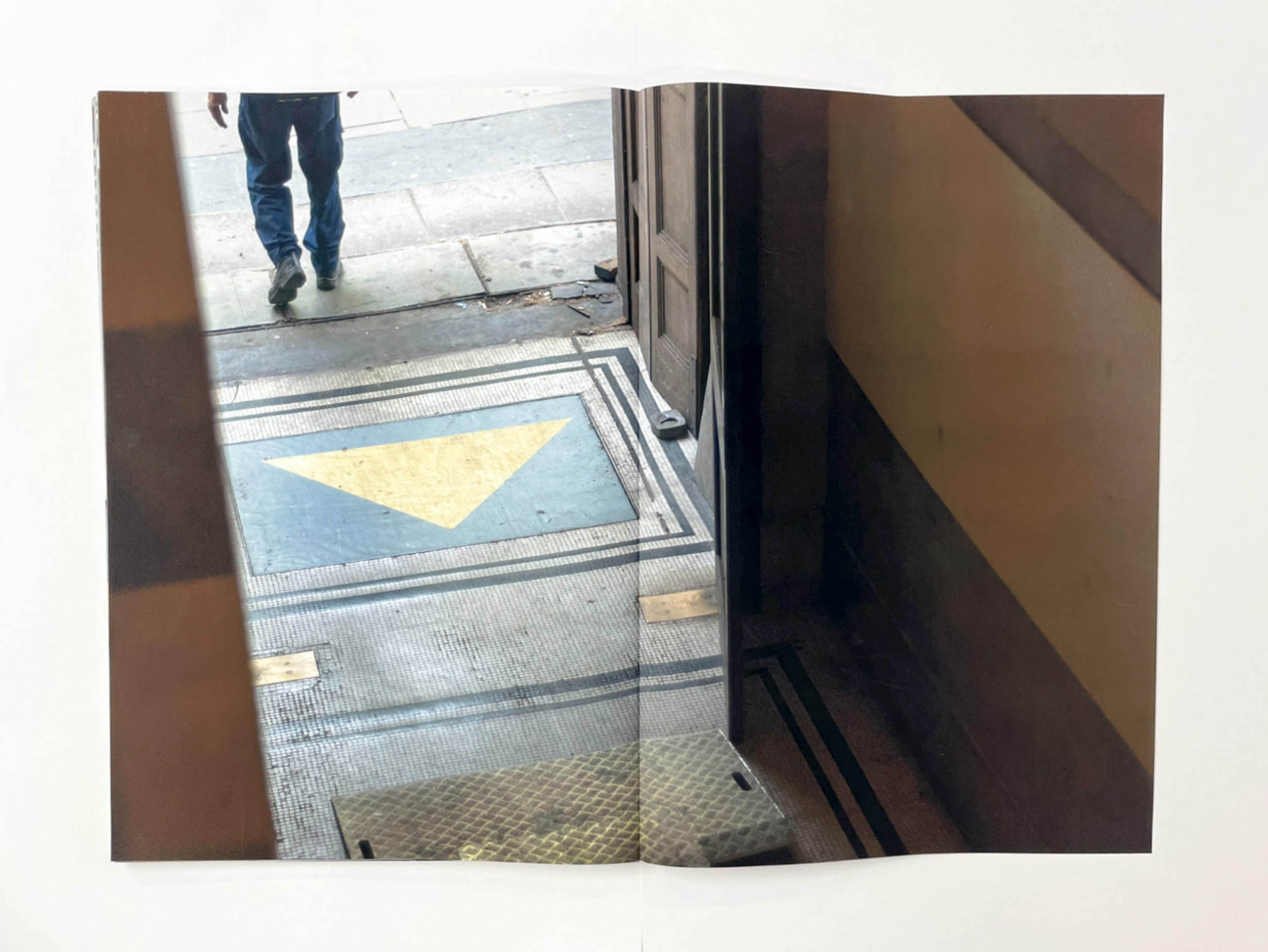 the mosaic floor of a corridor with a door opening onto a pavement on which a man in blue jeans is walking away