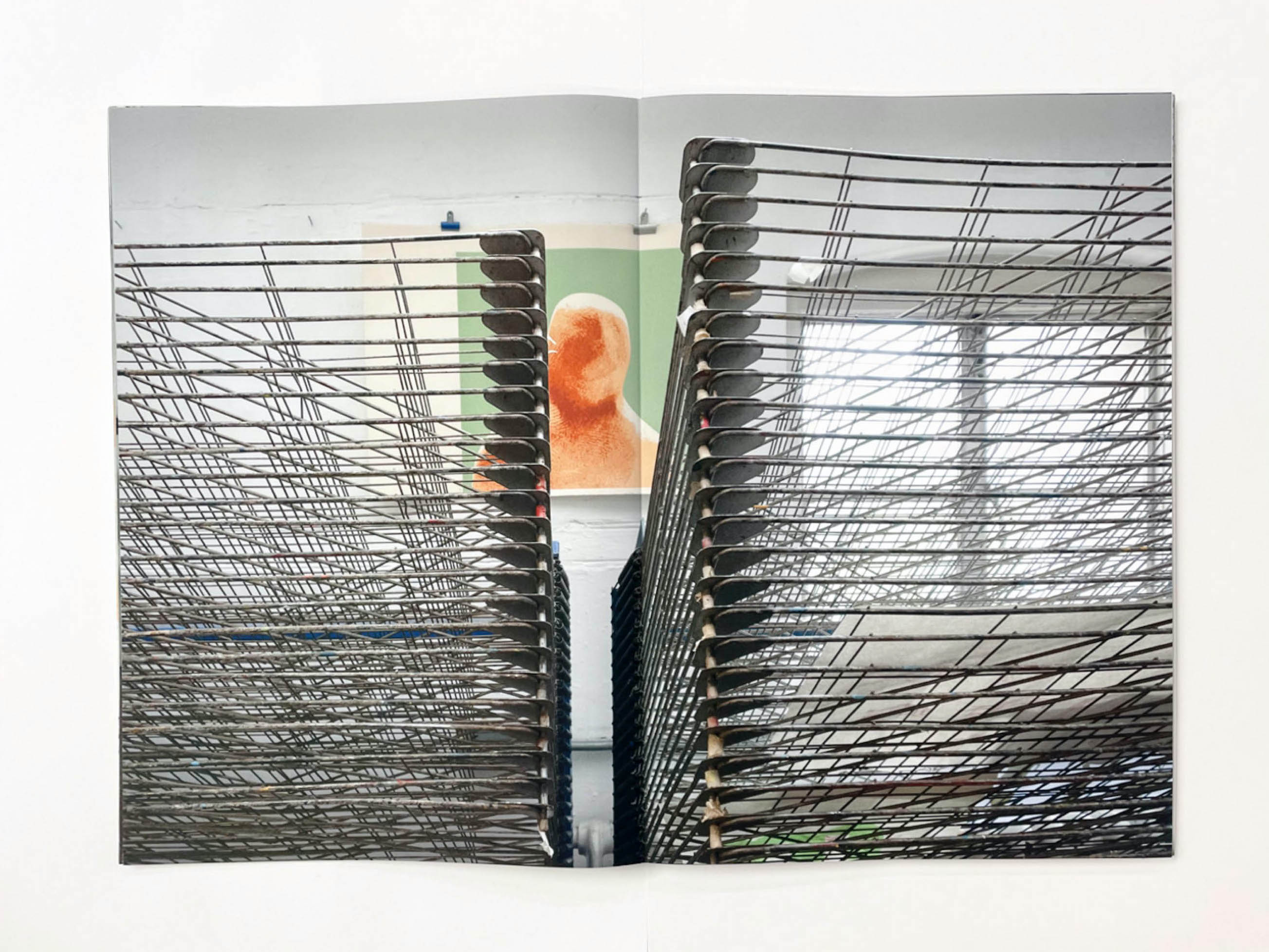 in between two wire drying racks an orange and green print of a head and shoulders without features is stuck to a white wall