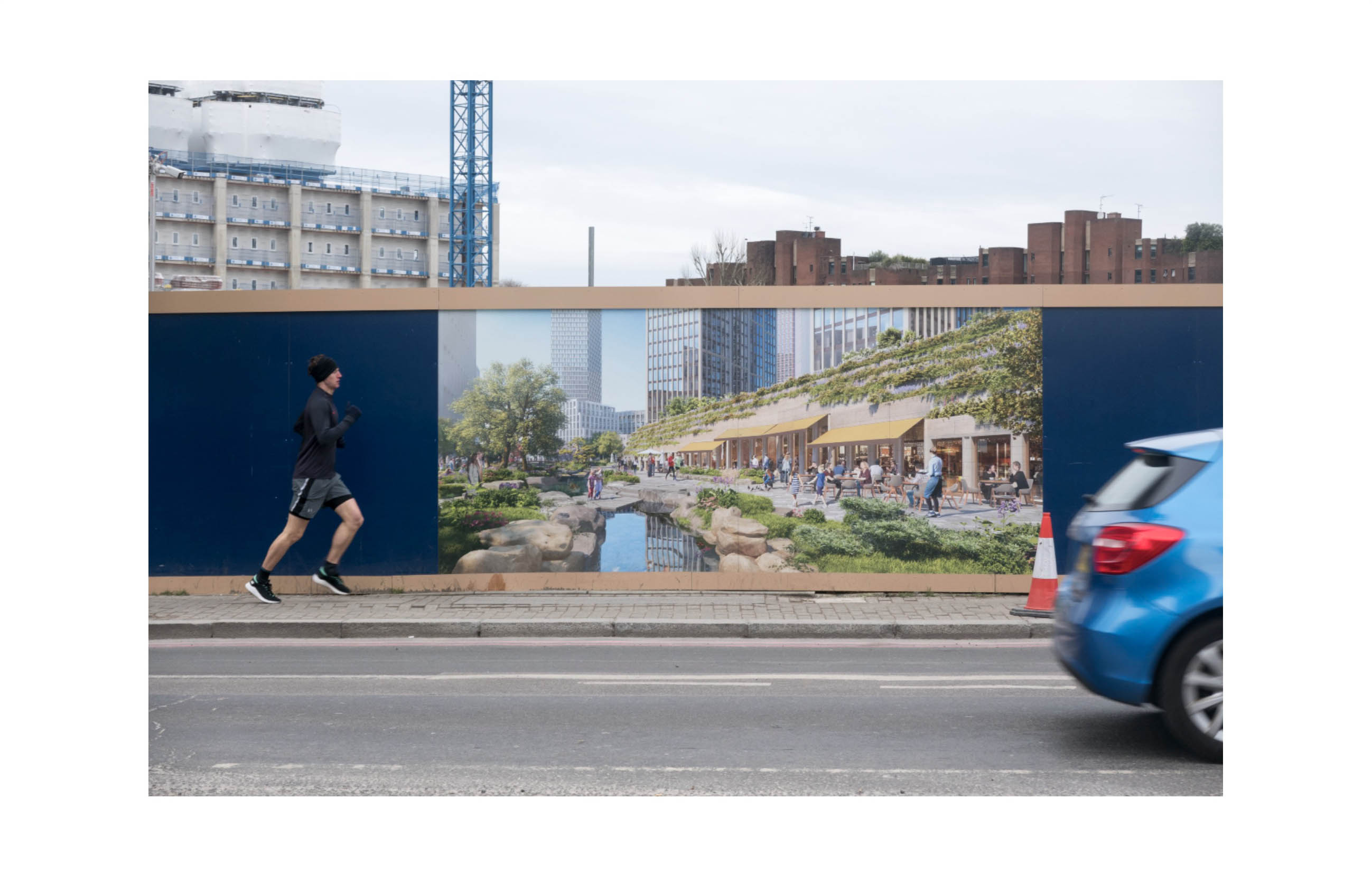 a hoarding shows a computer generated view of people at leisure in front of a rock pool with tall buildings rising behind; meanwhile in real life a runner and car pass in front and a grey sky looms behind