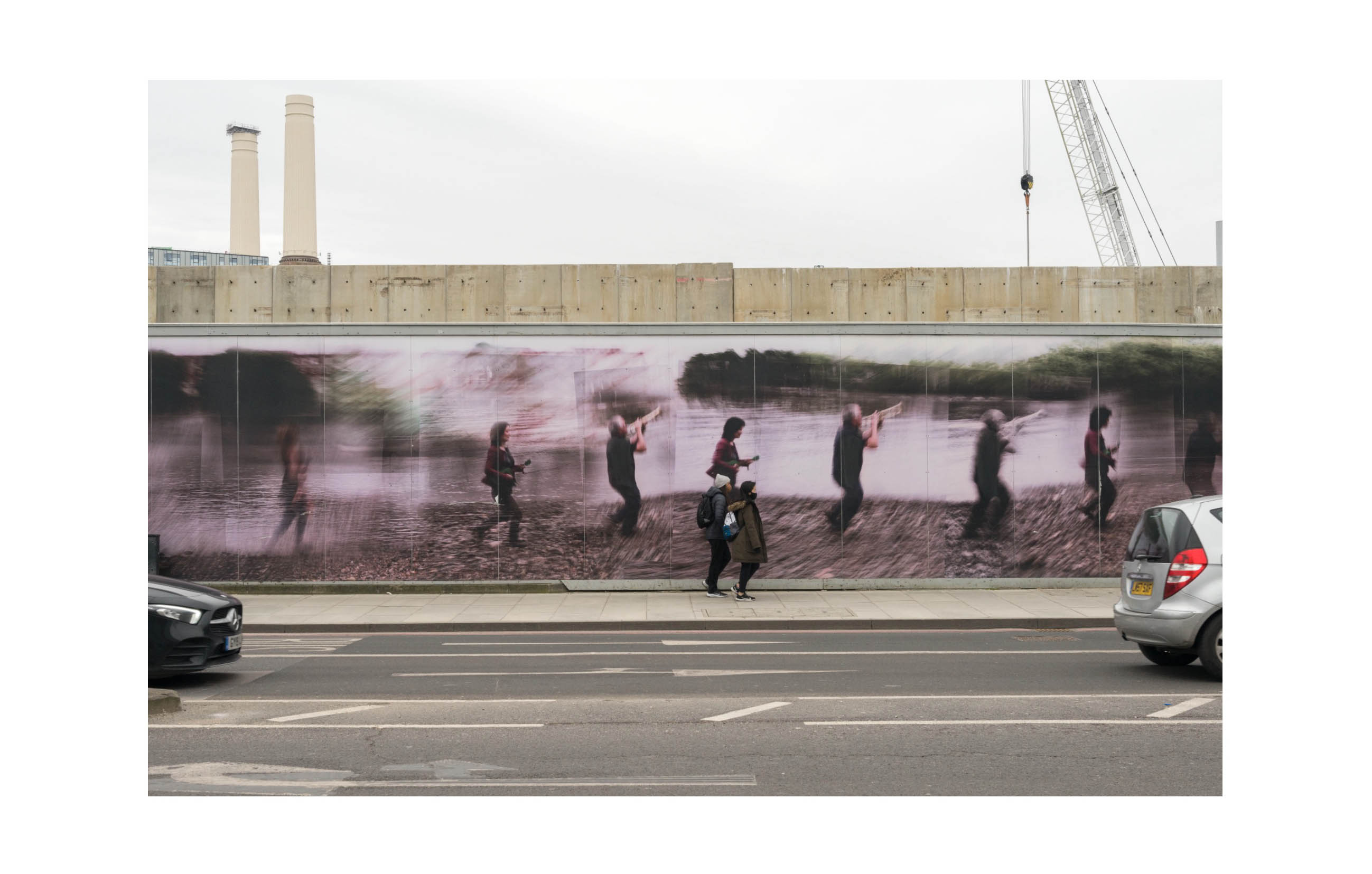 a long hoarding shows an artistic photo collage of blurred figures playing musical instruments alongside the Thames; in real life cars and people pass by in front