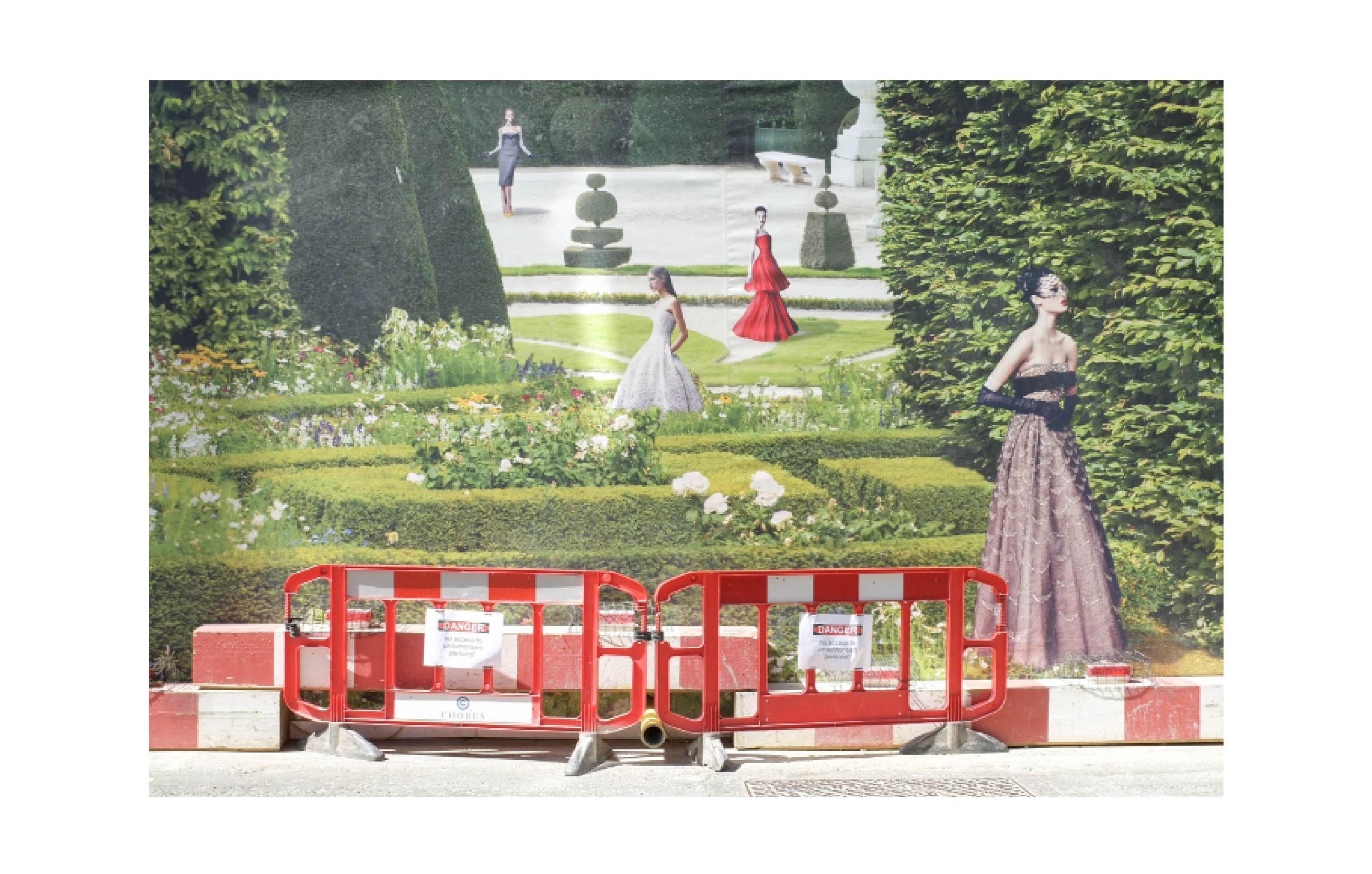 a hoarding shows four slender women in differently coloured evening gowns in a country house-style garden