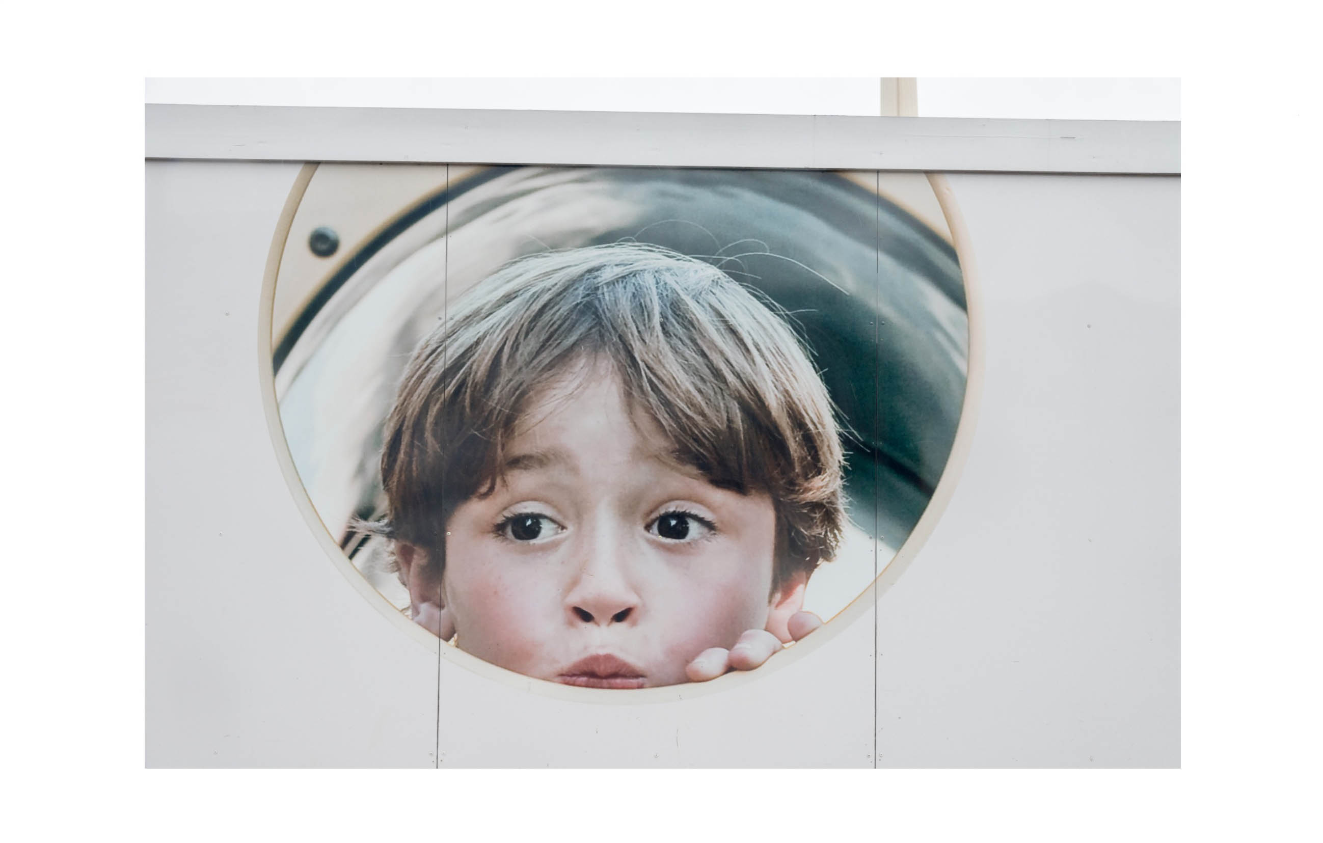 A hoarding shows a photographic image of an apparently privileged young boy peeping through a circular hole