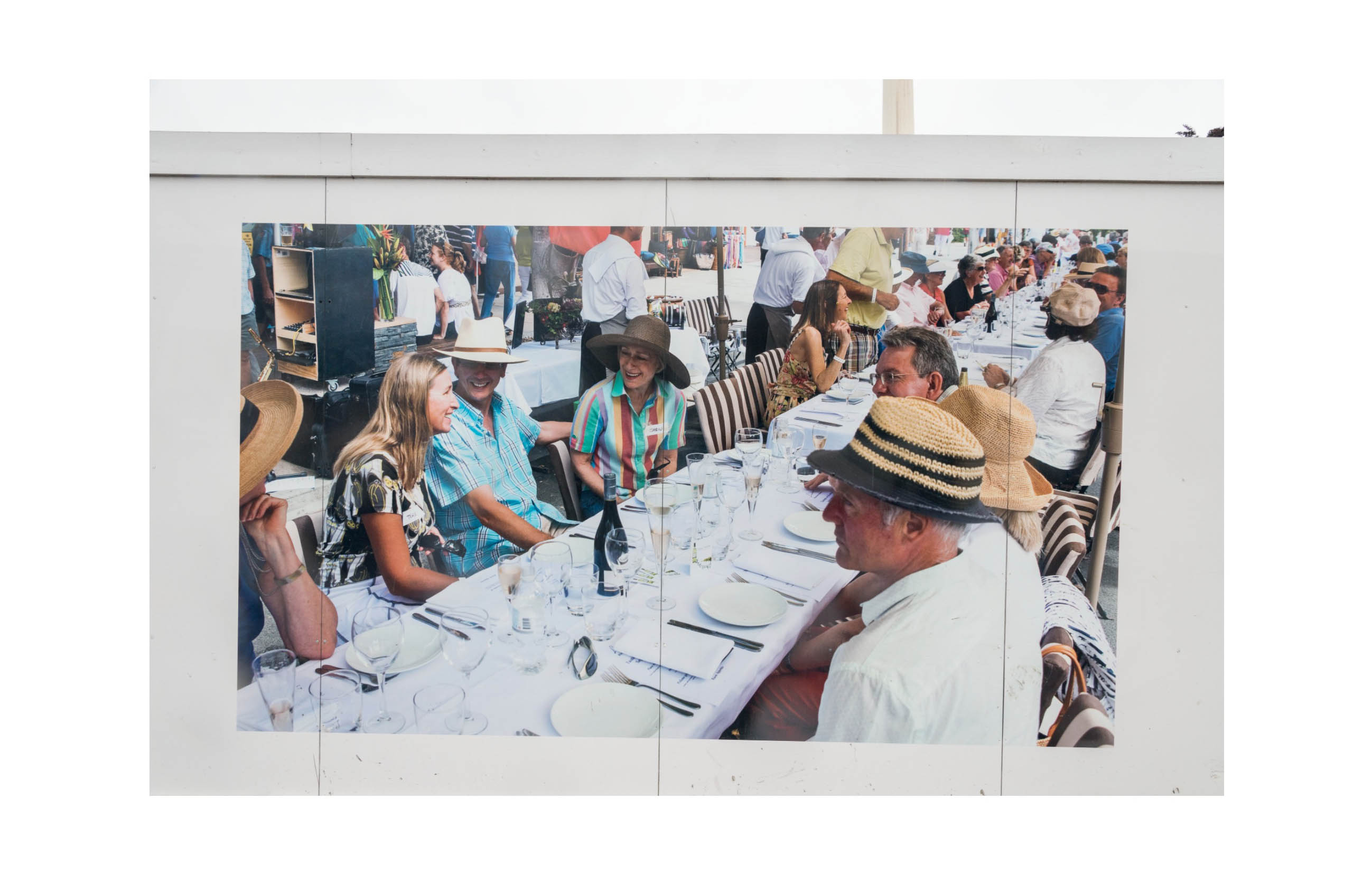 A hoarding shows a large outdoor dinner party with middle class white people