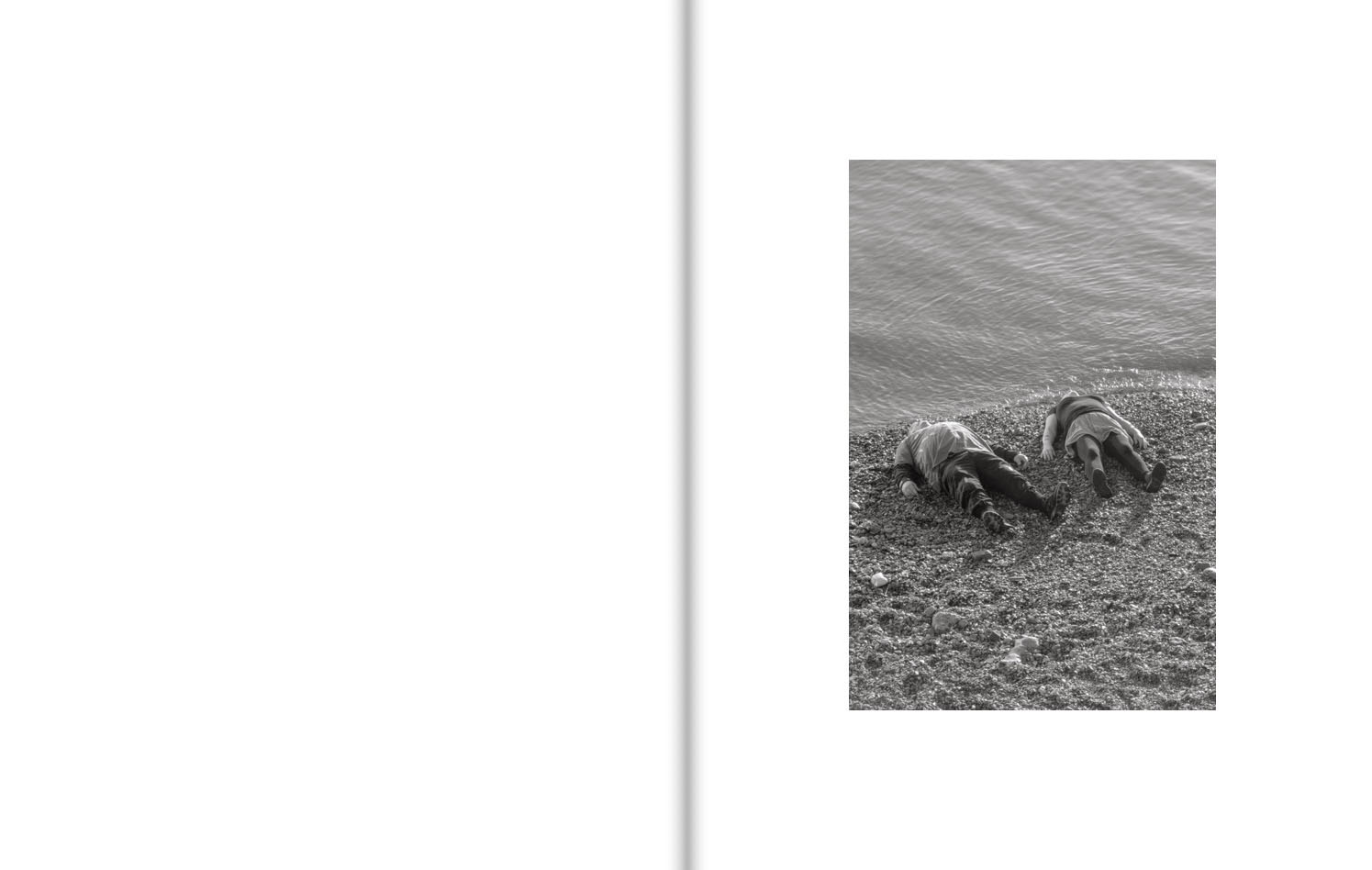 Two fully-clothed people lie on their backs on a shingle beach, their heads almost touching the water.