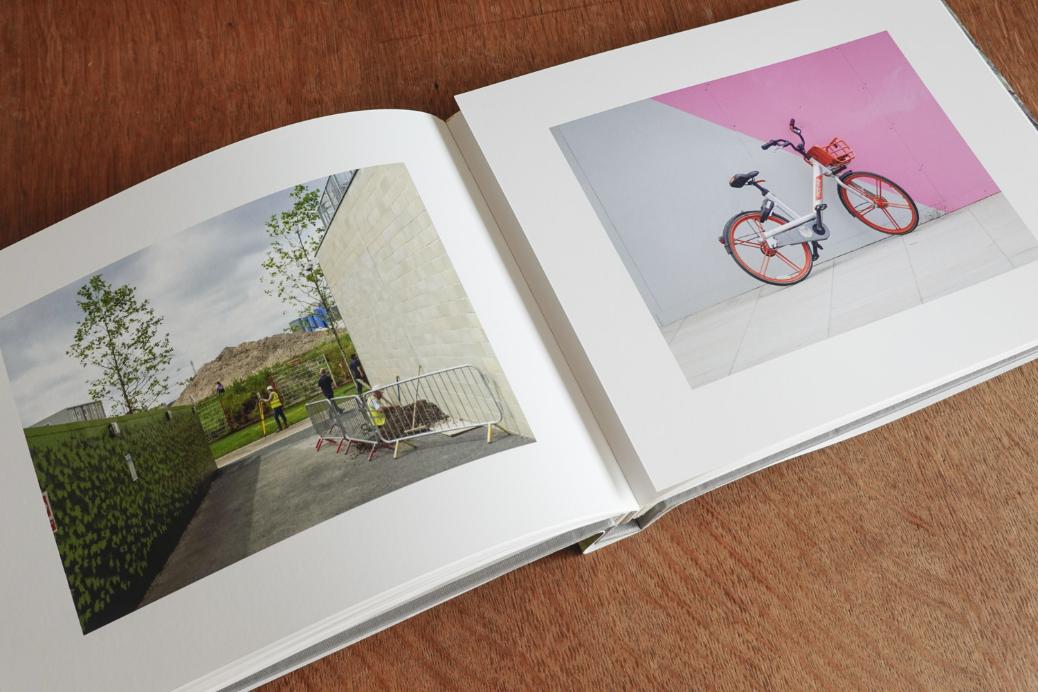 open books shows two photographs, one shows a scene with a surveyor in front of a large mound of earht, the other a rental bike stands against a pink and grey wall