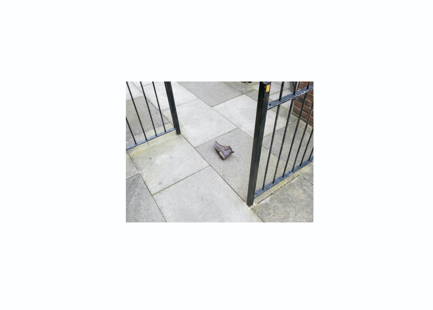 A photo of a discarded brown boot on a pavement between two railings