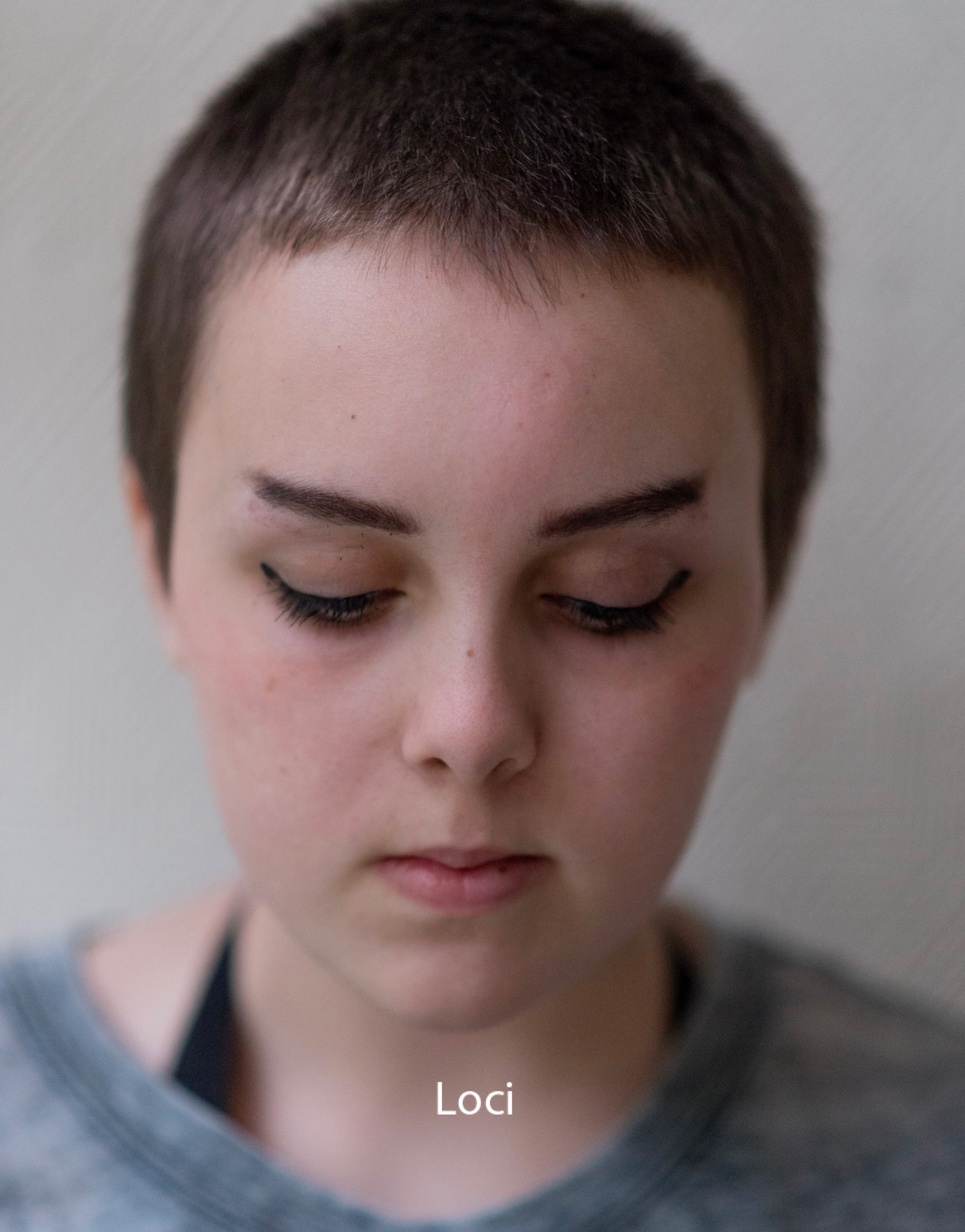 a close-up portrait of a young person looking downward with the title Loci overlaid