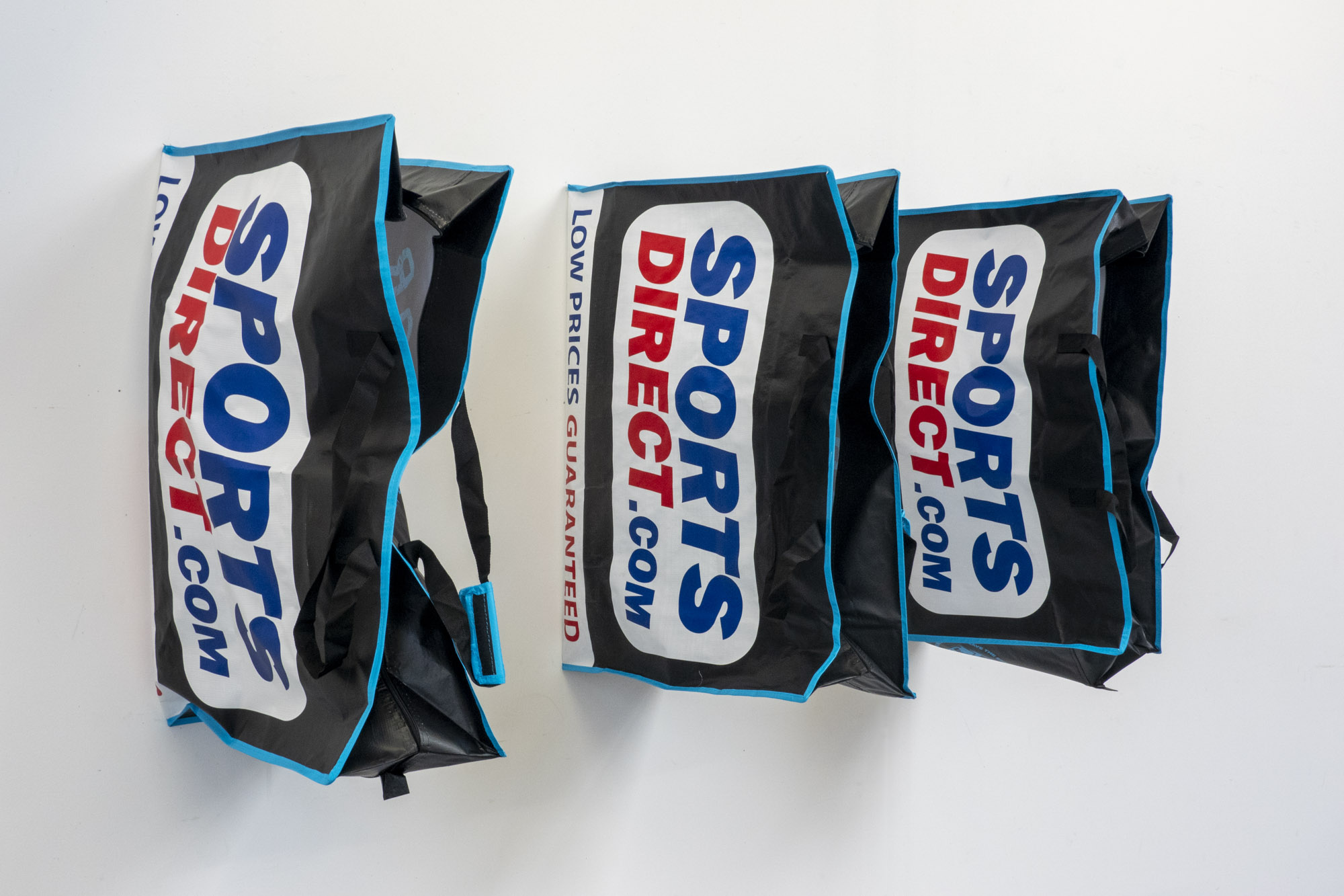 three large Sports Direct bags pinned in a row to a white wall