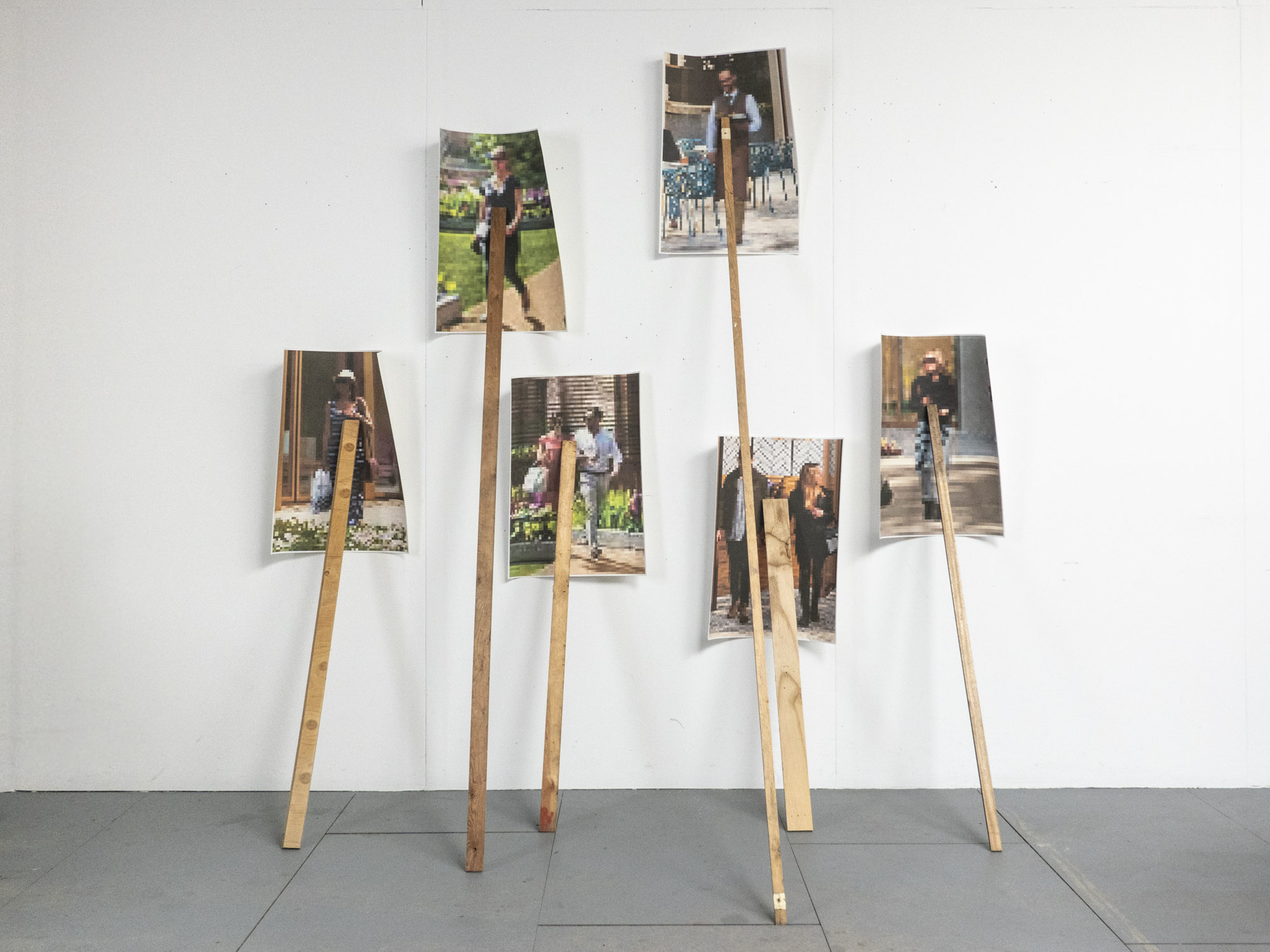 six images of people walking are held against a white wall by old pieces of wood