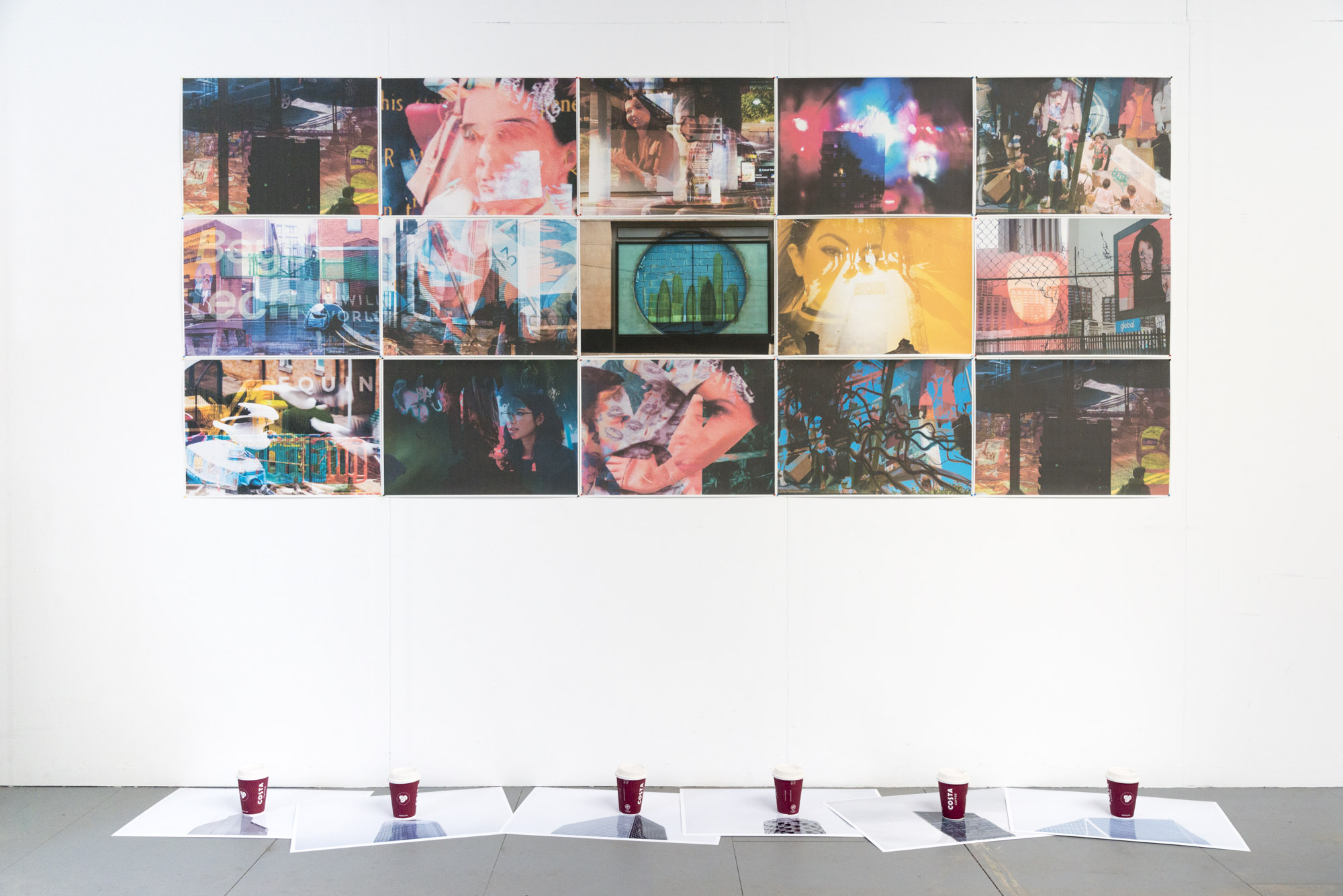 fifteen collaged photographs in a grid on a wall, on the floor beneath them are strewn six photos of the tops of skyscrapers, at the centre of each image is a Costa coffee cup