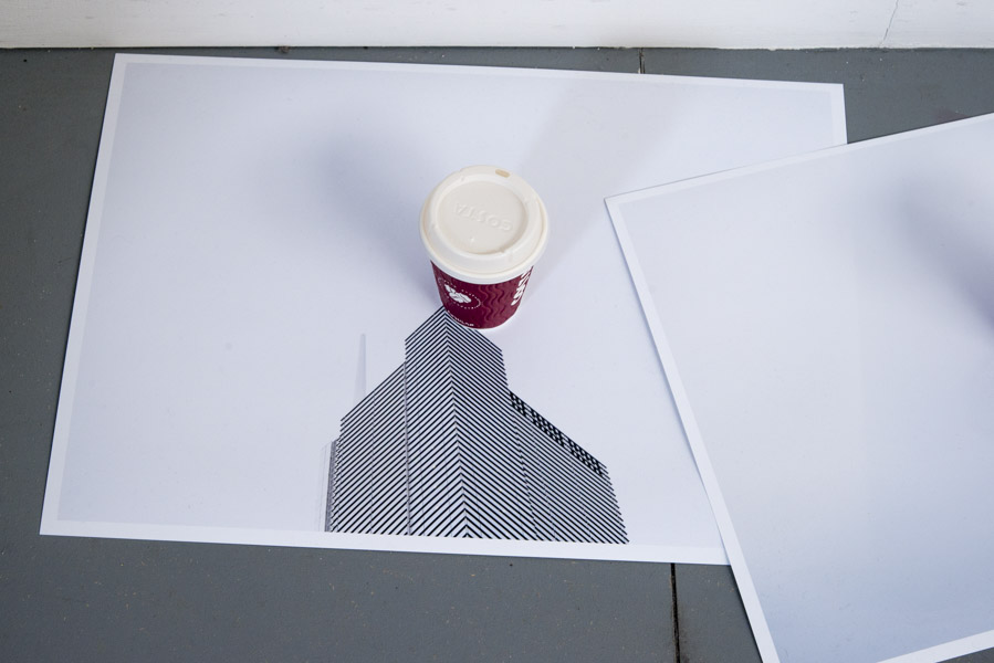 a close-up view of the first colour print on glossy paper of the top of a skyscraper against a grey sky, in the centre of which is a Costa coffee cup