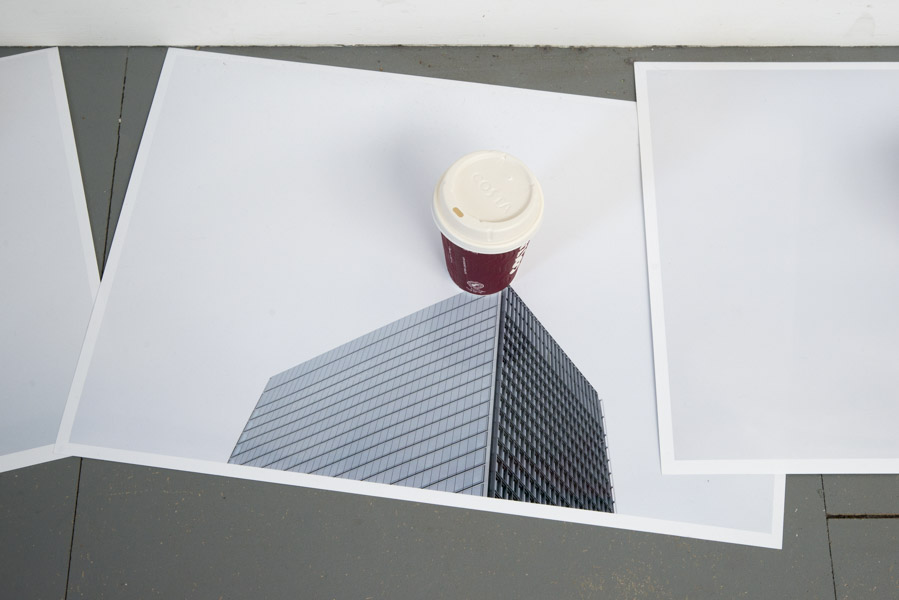 a close-up view of the third print on glossy paper of the top of a skyscraper, in the centre of which is a Costa coffee cup
