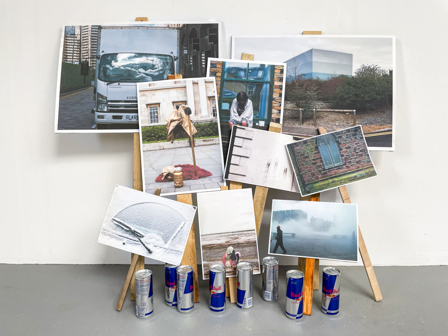 a view of the six large glossy photographic prints of the tops of skyscrapers strewn on the floor below the grid of images, at the centre of each print stands a Costa coffee cup